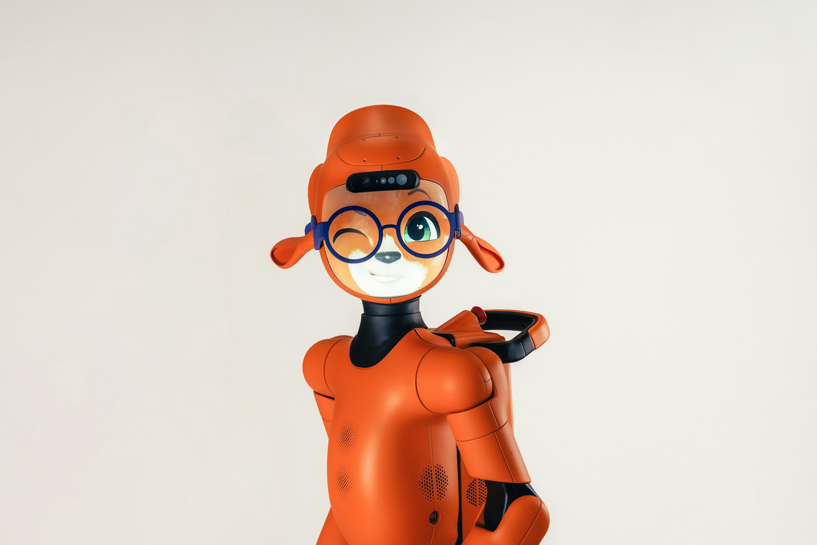 An orange humanoid robot with a digital face wearing blue glasses