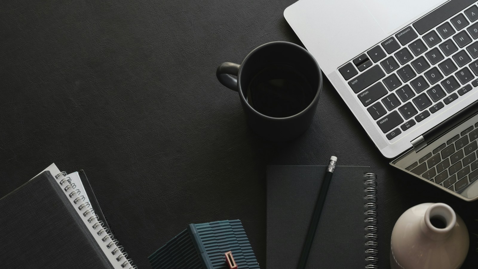 Laptop, mug, and notebooks on a dark workspace